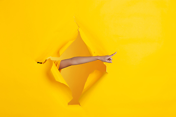 Image showing Female hand pointing in torn yellow paper hole background, celebration