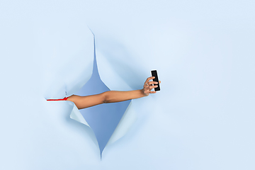 Image showing Female hand giving smartphone in torn blue paper hole background, celebration