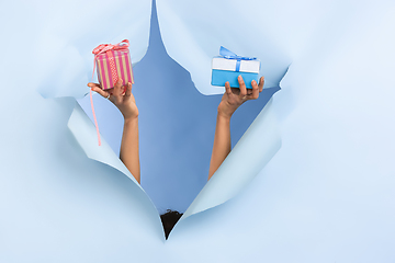 Image showing Female hand giving gift in torn blue paper hole background, celebration