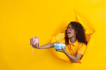 Image showing Cheerful young woman poses in torn yellow paper hole background, emotional and expressive