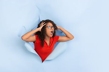 Image showing Cheerful young woman poses in torn blue paper hole background, emotional and expressive