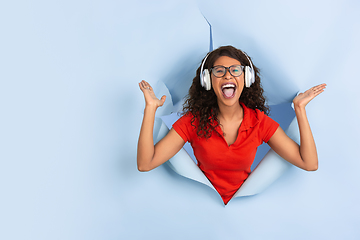 Image showing Cheerful young woman poses in torn blue paper hole background, emotional and expressive