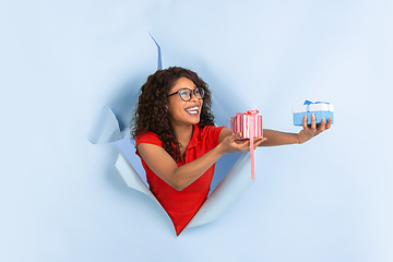 Image showing Cheerful young woman poses in torn blue paper hole background, emotional and expressive