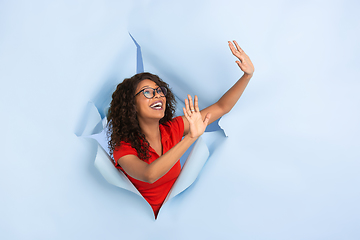 Image showing Cheerful young woman poses in torn blue paper hole background, emotional and expressive