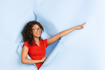 Image showing Cheerful young woman poses in torn blue paper hole background, emotional and expressive