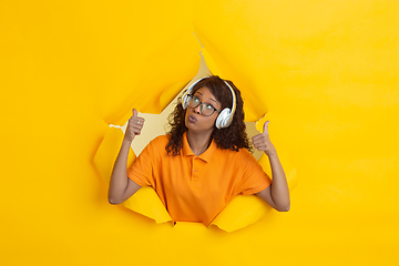 Image showing Cheerful young woman poses in torn yellow paper hole background, emotional and expressive