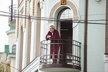 Image showing Mature senior older man during quarantine, realizing how important stay at home during virus outbreak, drinking coffee on the balcony