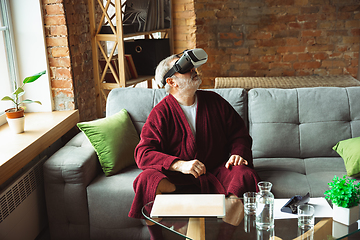 Image showing Mature senior older man during quarantine, realizing how important stay at home during virus outbreak, trying on VR-headset, playing, watching