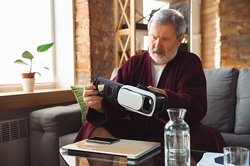 Image showing Mature senior older man during quarantine, realizing how important stay at home during virus outbreak, trying on VR-headset, playing, watching