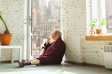 Image showing Mature senior older man during quarantine, realizing how important stay at home during virus outbreak, looking throught window on day New York city