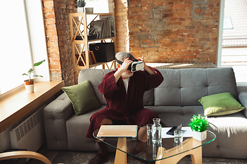 Image showing Mature senior older man during quarantine, realizing how important stay at home during virus outbreak, trying on VR-headset, playing, watching