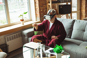 Image showing Mature senior older man during quarantine, realizing how important stay at home during virus outbreak, trying on VR-headset, playing, watching