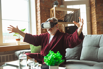 Image showing Mature senior older man during quarantine, realizing how important stay at home during virus outbreak, trying on VR-headset, playing, watching