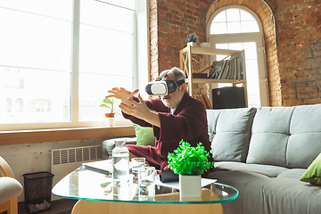 Image showing Mature senior older man during quarantine, realizing how important stay at home during virus outbreak, trying on VR-headset, playing, watching