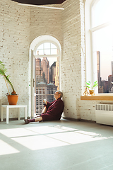 Image showing Mature senior older man during quarantine, realizing how important stay at home during virus outbreak, looking throught window on day New York city