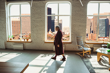 Image showing Mature senior older man during quarantine, realizing how important stay at home during virus outbreak, looking throught window on day Boston city