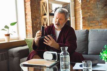 Image showing Mature senior older man during quarantine, realizing how important stay at home during virus outbreak, trying on VR-headset, playing, watching