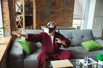 Image showing Mature senior older man during quarantine, realizing how important stay at home during virus outbreak, trying on VR-headset, playing, watching