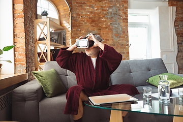 Image showing Mature senior older man during quarantine, realizing how important stay at home during virus outbreak, trying on VR-headset, playing, watching