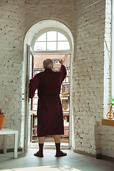 Image showing Mature senior older man during quarantine, realizing how important stay at home during virus outbreak, looking throught window on day city in France