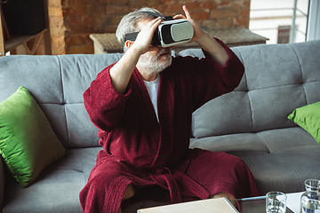 Image showing Mature senior older man during quarantine, realizing how important stay at home during virus outbreak, trying on VR-headset, playing, watching
