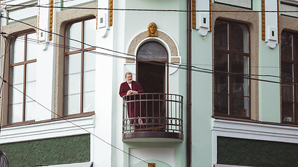 Image showing Mature senior older man during quarantine, realizing how important stay at home during virus outbreak, drinking coffee on the balcony