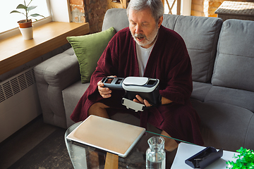 Image showing Mature senior older man during quarantine, realizing how important stay at home during virus outbreak, trying on VR-headset, playing, watching