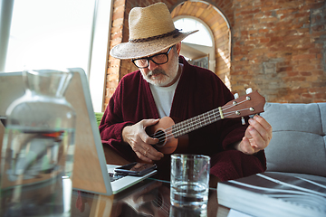 Image showing Mature senior older man during quarantine, realizing how important stay at home during virus outbreak, giving concert of taking online lessons of guitar playing in Monte Carlo