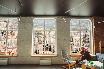 Image showing Mature senior older man during quarantine, realizing how important stay at home during virus outbreak, looking throught window on day city Monaco