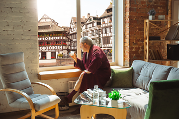 Image showing Mature senior older man during quarantine, realizing how important stay at home during virus outbreak, looking throught window on day city in France