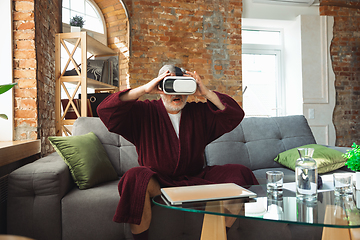 Image showing Mature senior older man during quarantine, realizing how important stay at home during virus outbreak, trying on VR-headset, playing, watching