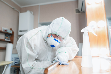 Image showing Coronavirus Pandemic. A disinfector in a protective suit and mask sprays disinfectants in the house or office