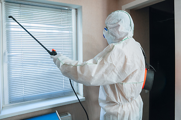 Image showing Coronavirus Pandemic. A disinfector in a protective suit and mask sprays disinfectants in the house or office