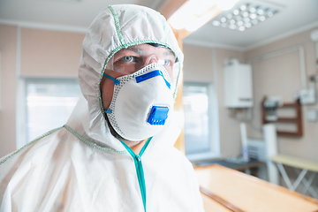 Image showing Coronavirus Pandemic. A disinfector in a protective suit and mask sprays disinfectants in the house or office