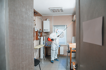 Image showing Coronavirus Pandemic. A disinfector in a protective suit and mask sprays disinfectants in the house or office