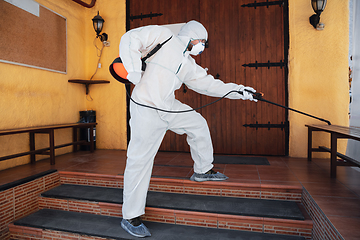 Image showing Coronavirus Pandemic. A disinfector in a protective suit and mask sprays disinfectants in the house or office