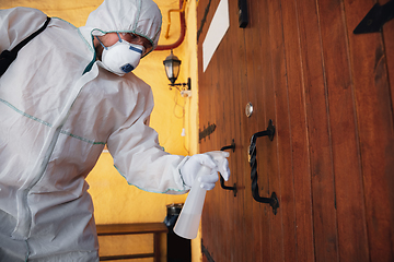 Image showing Coronavirus Pandemic. A disinfector in a protective suit and mask sprays disinfectants in the house or office