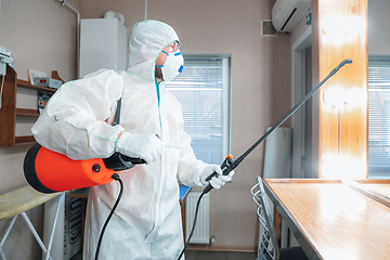 Image showing Coronavirus Pandemic. A disinfector in a protective suit and mask sprays disinfectants in the house or office