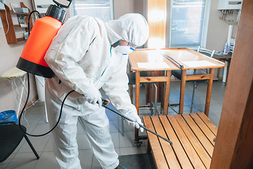 Image showing Coronavirus Pandemic. A disinfector in a protective suit and mask sprays disinfectants in the house or office