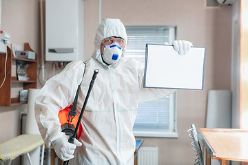 Image showing Coronavirus Pandemic. A disinfector in a protective suit and mask sprays disinfectants in the house or office