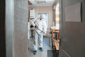 Image showing Coronavirus Pandemic. A disinfector in a protective suit and mask sprays disinfectants in the house or office