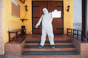 Image showing Coronavirus Pandemic. A disinfector in a protective suit and mask sprays disinfectants in the house or office