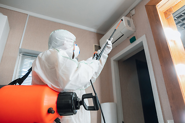 Image showing Coronavirus Pandemic. A disinfector in a protective suit and mask sprays disinfectants in the house or office