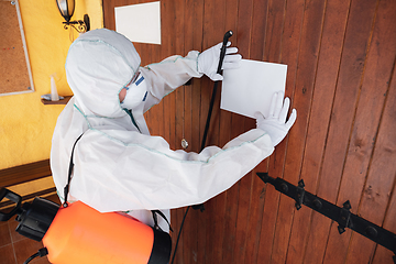 Image showing Coronavirus Pandemic. A disinfector in a protective suit and mask sprays disinfectants in the house or office