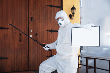 Image showing Coronavirus Pandemic. A disinfector in a protective suit and mask sprays disinfectants in the house or office