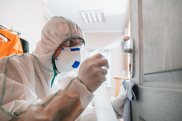 Image showing Coronavirus Pandemic. A disinfector in a protective suit and mask sprays disinfectants in the house or office