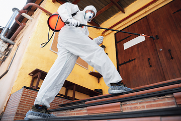 Image showing Coronavirus Pandemic. A disinfector in a protective suit and mask sprays disinfectants in the house or office