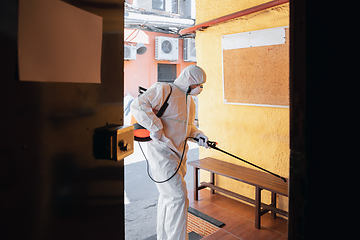 Image showing Coronavirus Pandemic. A disinfector in a protective suit and mask sprays disinfectants in the house or office