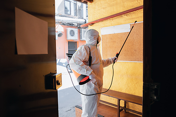 Image showing Coronavirus Pandemic. A disinfector in a protective suit and mask sprays disinfectants in the house or office