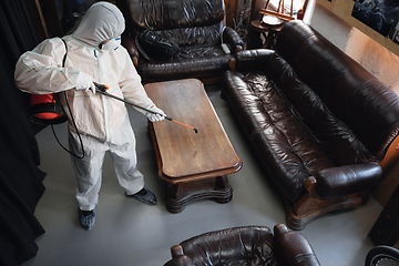 Image showing Coronavirus Pandemic. A disinfector in a protective suit and mask sprays disinfectants in the house or office